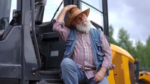 勤劳疲惫的老农坐在拖拉机上 脱下草帽慢吞吞地挥动着 有信心的英俊白人老人的画像 收割有休息的庄稼 — 图库视频影像