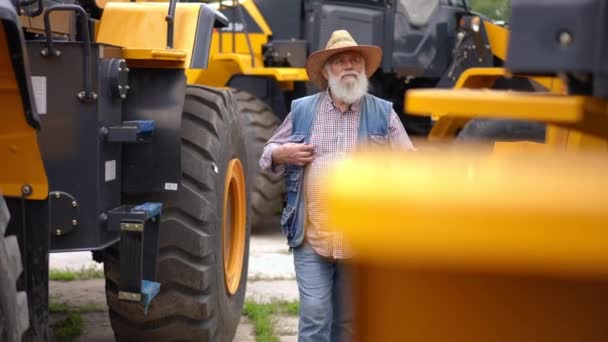 有自信而专注的老人在一排新的农用车辆之间选择新的拖拉机的画像 专业的高加索农民专家在室外购买耕作机 — 图库视频影像