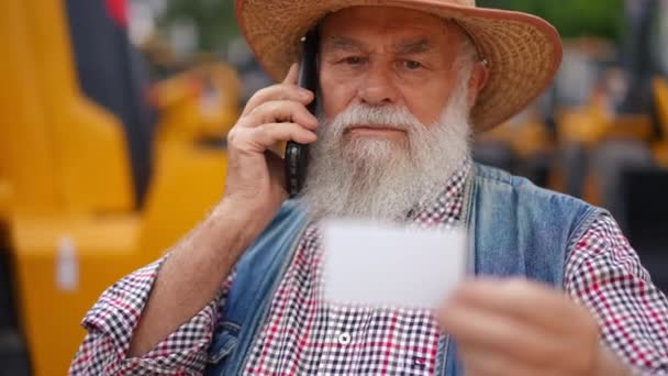Rack Fokus Från Koncentrerad Senior Bonde Talar Telefon Till Visitkort — Stockvideo