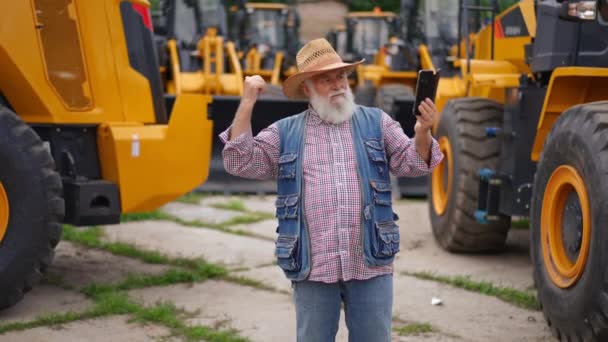 Старший Фермер Использующий Приложение Видеочата Телефоне Указывает Желтые Тракторы Продажи — стоковое видео