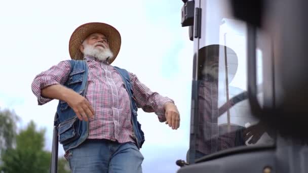 快乐的农民伸懒腰站在巨大的拖拉机旁边望着远方 满脸胡须的白人老人笑着享受户外阴天的画像 — 图库视频影像