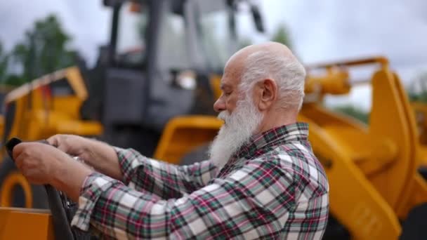 跟踪镜头侧视自信的老年人走向巨大的黄色拖拉机放置工具包选择设备进行慢动作修理 白人男性工程师修理农用车辆 — 图库视频影像