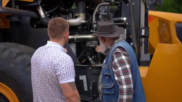 回顾年轻和年长的白人男人在外面谈论检查新型拖拉机的情景 有自信的农民经验 帮助农学家选择农业车辆 慢动作 — 图库视频影像