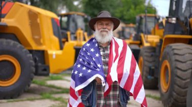 Canlı kamera, tarımsal makine pazarında poz veren Amerikan bayrağındaki kendinden emin yaşlı adama odaklan. Ön cephede profesyonel deneyimli beyaz çiftçi açık havada