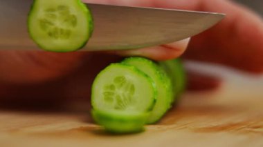 Kesme tahtasına bıçak saplanmış aşırı yakın plan yeşil salatalık. Yakın plan beyaz kadın elleri evde salata için sebze kesiyor.