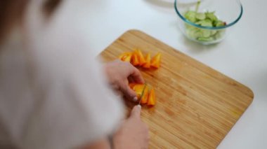 Tanımlanamayan genç bir kadının omzundan ateş etmek domates doğramak salatalıkla kabın içine malzeme koymak. Kafkasyalı ev hanımı evde mutfakta lezzetli salata pişiriyor.
