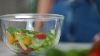 Kapalı çekimde ayçiçeği zeytinyağını taze organik salatayla yavaş çekimde kaseye boşaltıyorum. Yakından tanınmayan beyaz bir kadın akşam yemeği için leziz bir öğle yemeği hazırlıyor.