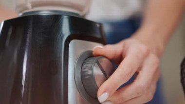Yakın plan kadın eli blender 'ın düğmesini çeviriyor smoothie karıştırıyor ve sağlıklı içecekle ayrılıyor. Tanımlanamayan Kafkasyalı genç bayan evde lezzetli bir öğle yemeği hazırlıyor.