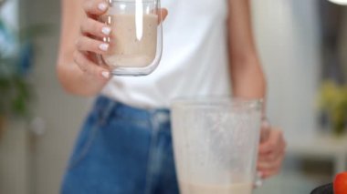 Tanımlanamayan bir kadın, kameraya yavaş çekimde lezzetli bir smoothie ile cam esnetiyor. Ön manzara. Beyaz kadın içeride lezzetli kokteyller gösteriyor.