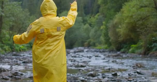 Carefree Woman Yellow Rain Coat Throwing Rocks Mountain River Slow — Stock Video