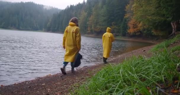 喀尔巴阡山脉的Synevyr湖开阔地拍摄 两名女徒步旅行者在海岸漫步 穿着黄色雨衣在阴沉沉的日子里行走的年轻女子充满自信 Cinema Prores — 图库视频影像