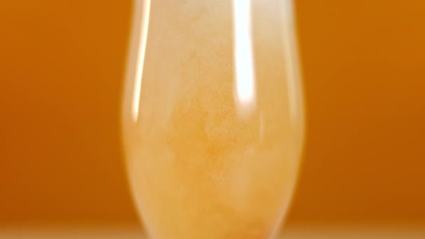 特写啤酒泡沫洒在橙色背景的玻璃杯上 盛装冷饮饮料做广告 — 图库视频影像