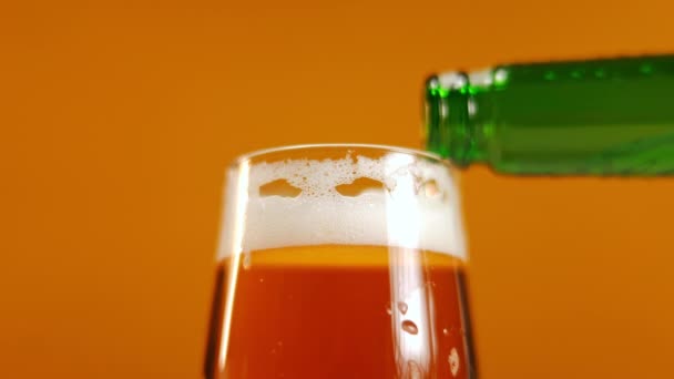 把啤酒从瓶子里倒进杯子里 然后离开 橙色背景白色泡沫的特写清爽酒精饮料 — 图库视频影像