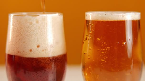 近视眼镜配上淡淡的啤酒和深色的啤酒 然后慢动作地倒入泡沫 橙色背景下的清凉饮料 — 图库视频影像