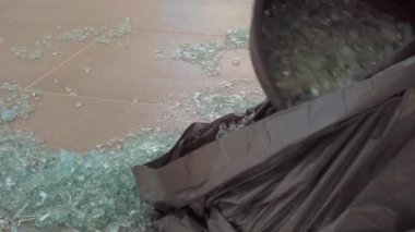Yakından tanınmayan bir kadın kırık cam topluyor çöp torbasında yemek artıklarını yerleştiriyor. Kapalı alanda yerleri temizleyen kadın elleri.