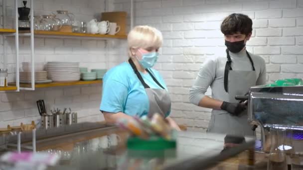 カフェで働く積極的な白人女性と顔のマスクの男がチャット笑顔 コーヒーハウスの職場で働く若い男女 サービス業の概念 — ストック動画