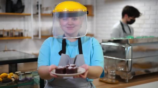 眼前的年轻女子在面罩伸展板与美味的甜点看着相机的微笑 白人雇员在室内咖啡店摆出食物姿势的画像 — 图库视频影像