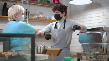 Yüz maskeli genç adam dirseklerine dokunan kadını selamlıyor ve gülümsüyor. Kafkas erkek çalışanı, kahve evinde bayan meslektaşıyla sohbet ediyor.