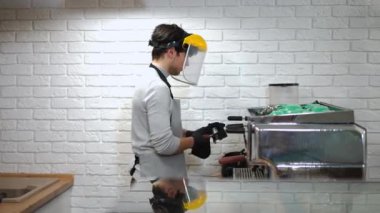 Kafedeki kahve makinesinin yüz koruyucu parçalarını temizleyen beyaz bir adamın yan görünüm portresi. Kahve dükkanında çalışan profesyonel bir baristanın orta boy fotoğrafı.