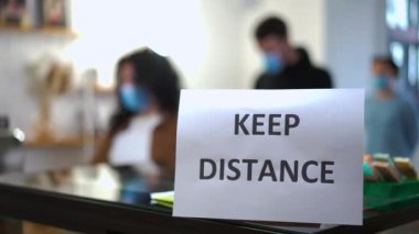 Yakın plan Mesafe tabelası. Arka planda kahve alan müşterilerin bulanık çizgisi. Koronavirüs salgını ile ilgili kafede kuyrukta bekleyen tanınmayan beyaz erkek ve kadınlar