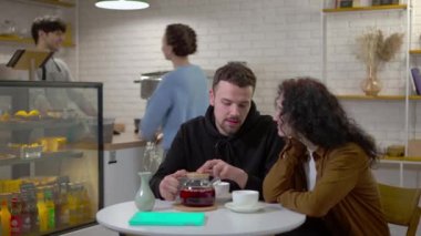 Sevgi dolu genç erkek arkadaş fincanlara çay dolduruyor kafede kız arkadaşıyla oturuyor arka planda barista 'dan sipariş veriyor. Kafkasyalı çift, şehir merkezindeki bir kafede flört ediyor. Eğlencenin tadını çıkarıyor.