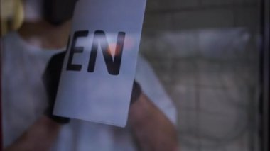 Erkek eller, kafe girişinde açık ile kapalı arasında kağıt çeviriyor. Yüzü maskeli ve eldivenli tanımlanamayan beyaz adam Coronavirus salgınıyla ilgili küçük işletmeyi kapatıyor.