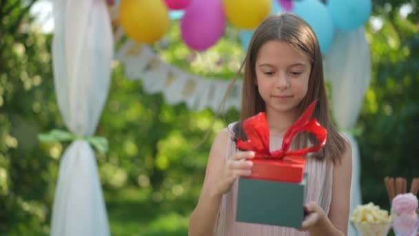 惊喜的生日女孩的肖像打开礼物 让人兴奋的面部表情 在阳光明媚的夏日 快乐的白人孩子在公园里庆祝节日 慢动作 — 图库视频影像
