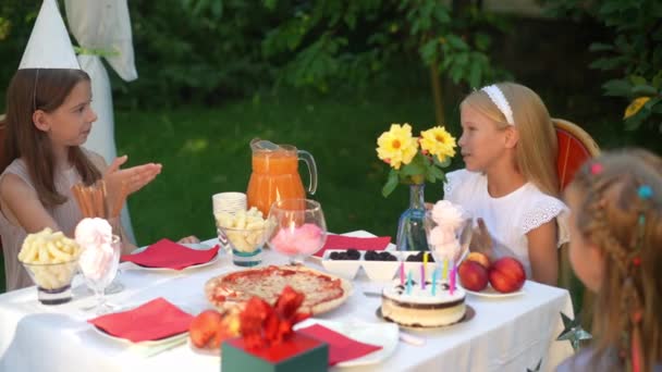 一个积极快乐的女孩带着大拇指 慢吞吞地和朋友聊天 坐在夏季公园的生日桌旁 白人儿童在户外欢度派对的肖像 — 图库视频影像