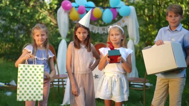 在夏日阳光明媚的公园里 心满意足的生日女孩和朋友们摆出慢动作的礼物 积极乐观的白人男孩和女孩在户外享受派对的正面肖像 — 图库视频影像