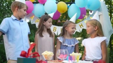 Bir grup mutlu ve rahat çocuk bahçede doğum gününü kutluyorlar. Dört pozitif beyaz kız ve oğlan yaz parkında ağır çekimde kucaklaşıyorlar.
