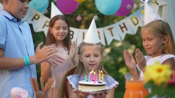 Mädchen Bläst Kerzen Auf Geburtstagstorte Aus Während Freunde Urlaub Jubelnd — Stockvideo