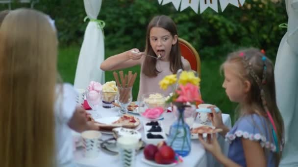 白人の女の子は屋外の友人と誕生日を祝うおいしい甘いケーキを食べる かわいい子供の肖像パーティーのテーブルに座っておいしいデザートを楽しんで — ストック動画
