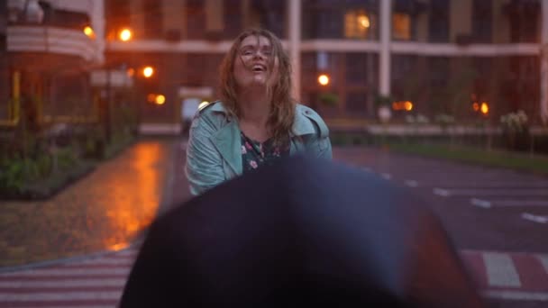 陽気プラスサイズの女性の夜の通りにゆっくりと動き カメラを見て笑みを浮かべて傘を回転立って 中出しフロントビューポートレートの白人幸せな女性ポーズ屋外で市 — ストック動画