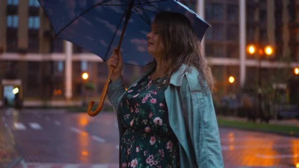 快乐的成年女人 带着雨伞慢吞吞地甩着头发 看着镜头微笑着在街上摆姿势 城市里快乐的白人加身材女士享受雨夜的画像 — 图库视频影像