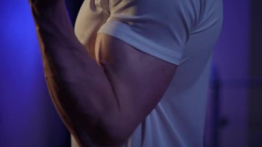 Kapalı alanda, karanlıkta, spor adamının kol kası halteri kaldırıyor. Yaklaştın. Tanınmaz hale geldin. Beyaz adam spor salonunda ekipmanla çalışıyor.