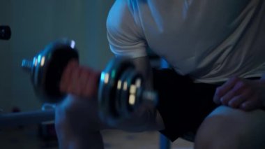 Tanınmaz haldeki güçlü sporcu, halterini kaldırıyor ve karanlıkta egzersiz masasında oturuyor. Genç beyaz kaslı adam spor salonunda kas çalıştırıyor.