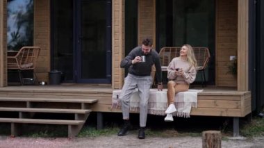 Verandada oturan adamla konuşan gülümseyen bir kadın erkek arkadaşı olarak tahta yazlığa giriyor. Kaygısız Kafkasyalı çift, sabah çayını dışarıda içiyor.