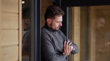 Kafkasyalı genç adam, verandadan ahşap eve giren cam kapıyı gözetliyor. Evde rahat yakışıklı bir adam var.