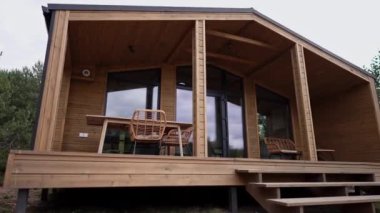 Tahta yazlık evde verandalı kameralar soldan sağa dönüyor. Terasta hasır mobilyalı kimse yok.