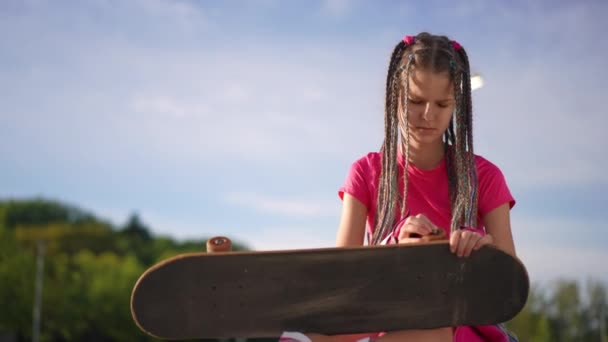 Εστιασμένη Έφηβος Κορίτσι Εξέταση Τροχό Του Skateboard Στέκεται Στην Ηλιόλουστη — Αρχείο Βίντεο