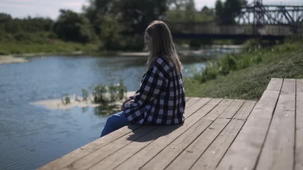 Przygnębiona Młoda Biała Kobieta Siedząca Drewnianym Pomoście Wrzucająca Kamienie Rzeki — Wideo stockowe
