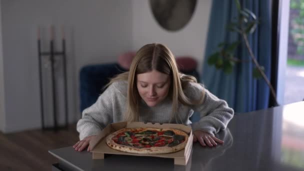 ミディアムショット幸せな若い女性はおいしいピザを舐め ゆっくりとした動きで微笑みます リビングルームの自宅でおいしい夕食とコーカサス美しい女性の肖像画 — ストック動画