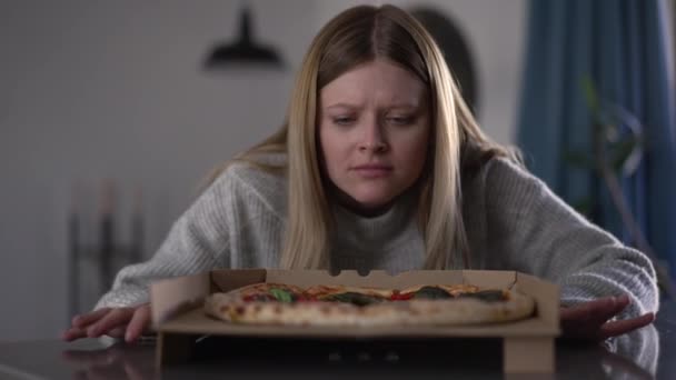 Mujer Joven Oliendo Pizza Con Expresión Facial Decepcionada Sentada Casa — Vídeo de stock