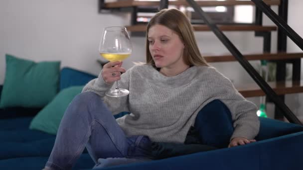ソファーの思考に座ってグラスに白ワインを塗った悲しい美しい女性 落ち込んでいる若い白人女性の肖像画 週末に家で屋内で一人で — ストック動画