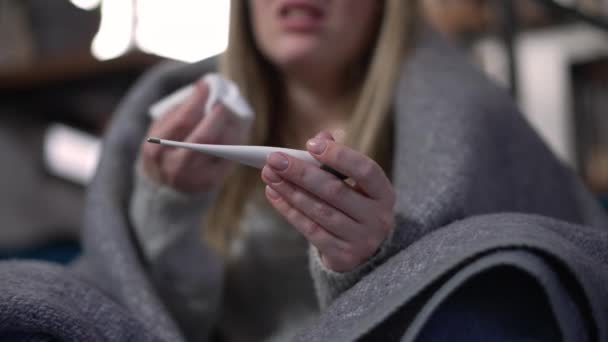 女性のコーカサス手のクローズアップ温度計は 背景で咳をするぼやけた女性と 室内でのウイルス感染の症状を有する認知できない若い病気の女性を閉じる — ストック動画