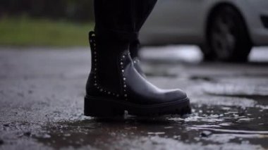 Yan manzara kadın bacakları su birikintisinde botları yıkıyor arabaya doğru yürüyor ve otomobilde oturuyor. Yakından tanınmayan genç, beyaz bir kadın yağmurlu bir havada arabaya biniyor.