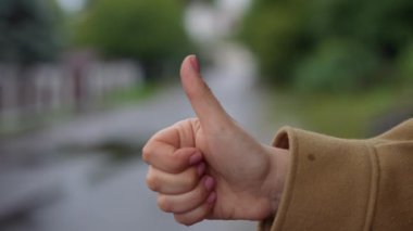 Yakından genç bir bayan el hareketi yaparak otostop çekiyor. Yakından tanınmayan beyaz kadın yağmurlu bir günde nakliye aracına yetişiyor.
