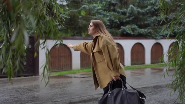 站在阴云密布的街道上的年轻白人黑发女人的侧视图画像 外面下雨天带着行李搭便车的迷人美女 — 图库视频影像