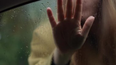 Kafkas kadın eli arabanın camında, yağmur damlalarıyla. Açık havada yağmurlu bir günde ağır çekimde cama dokunan bulanık, esmer bir kadın.