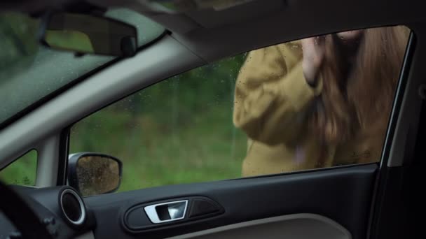 心配している女性は 屋外に立っている閉じた車の中を見ながら電話で話しています 自動車に問題がある不安な白人女性のガラスを通して撮影 — ストック動画